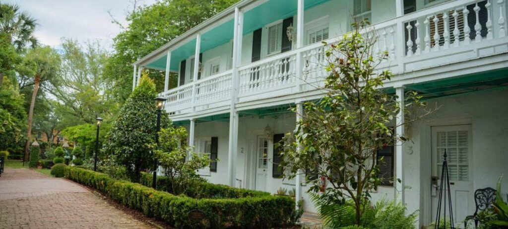 Exterior view of the Battery Carriage House surrounded by lush gardens, brick pathways, and classic Charleston architecture.