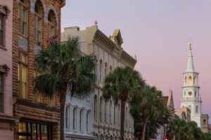 Historic Charleston streets lined with palm trees and classic architecture leading toward St. Michael's Church at sunset.
